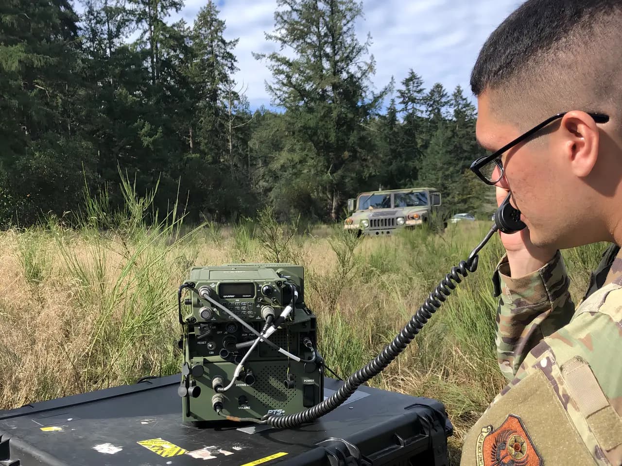 Operator on a radio handset with a docked tactical radio in the field